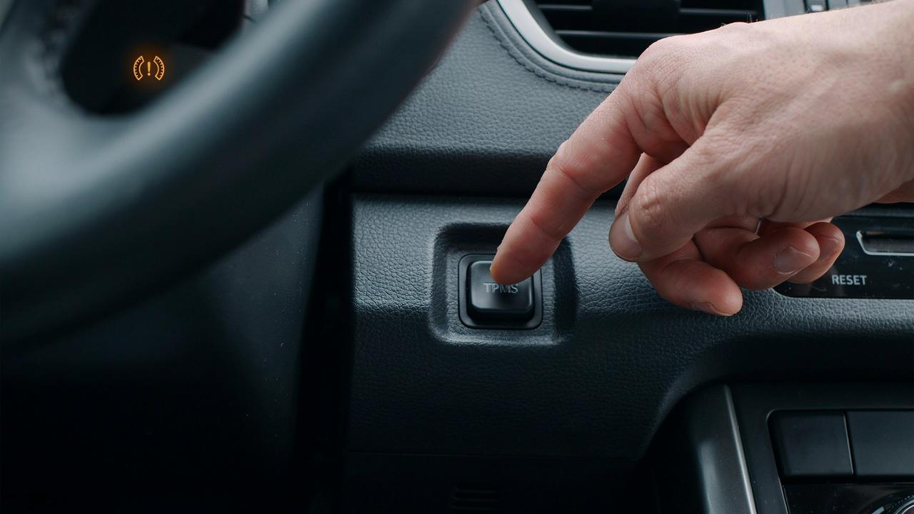 Pressing the TPMS reset button to clear the tire sensor warning.