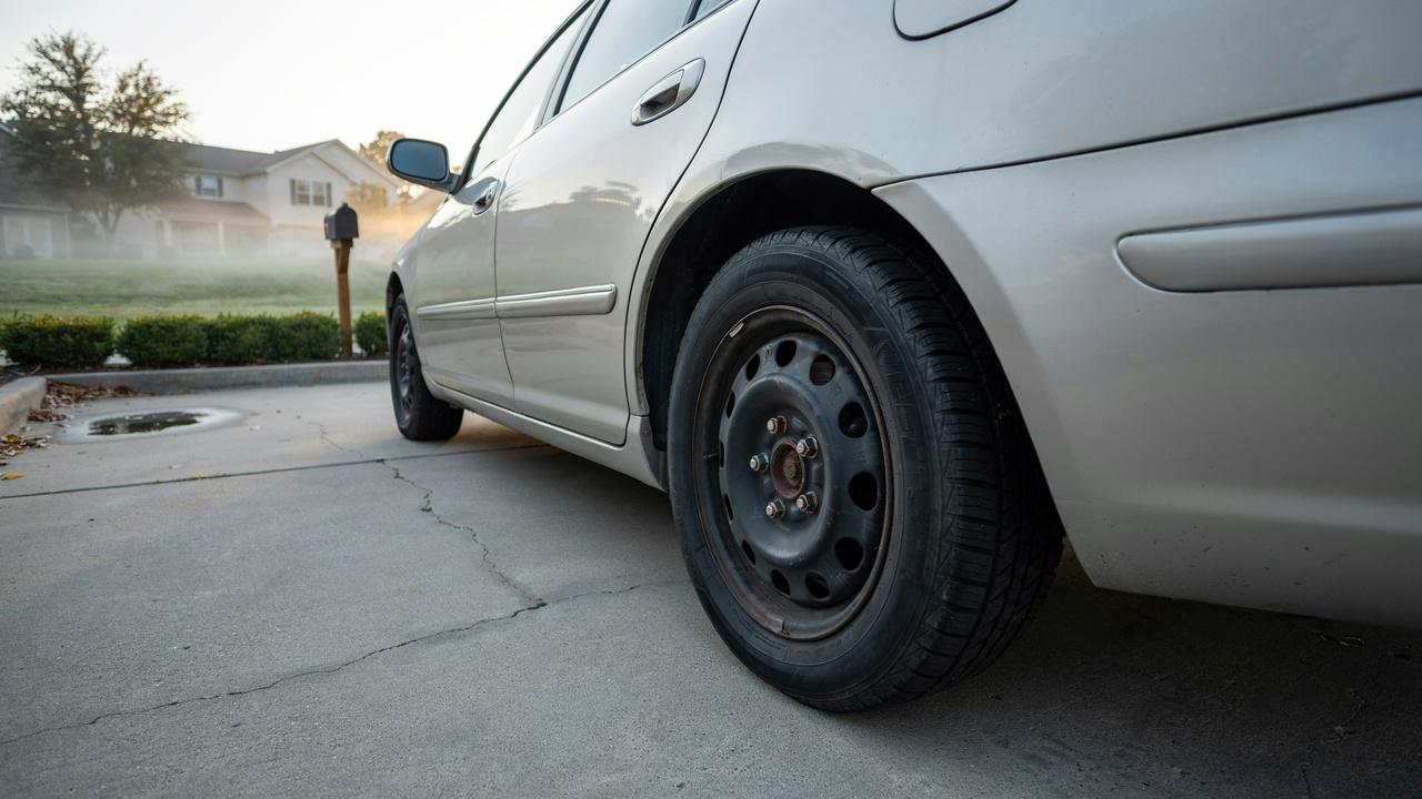 Driver inspecting a car tire that lost air overnight in a driveway.