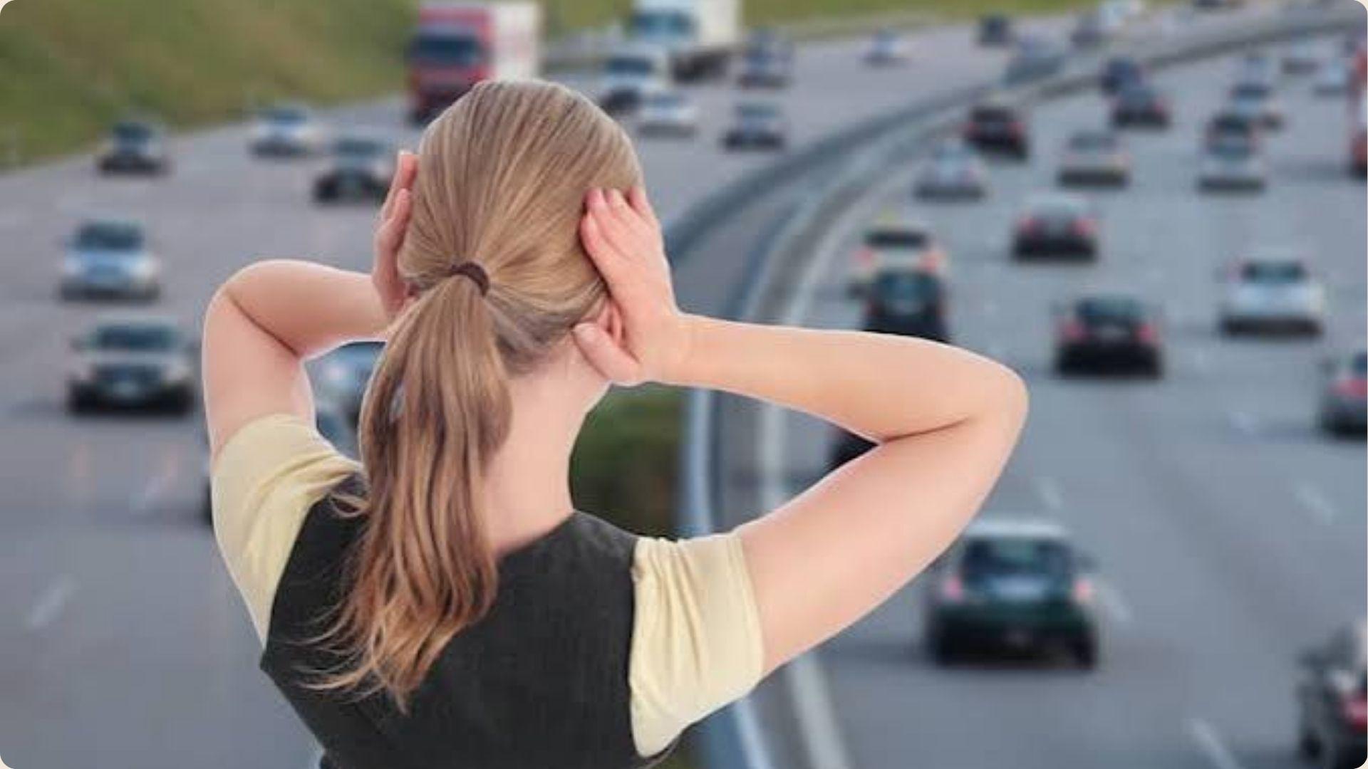 A woman gazes at the busy highway, observing the flow of traffic and vehicles passing by.