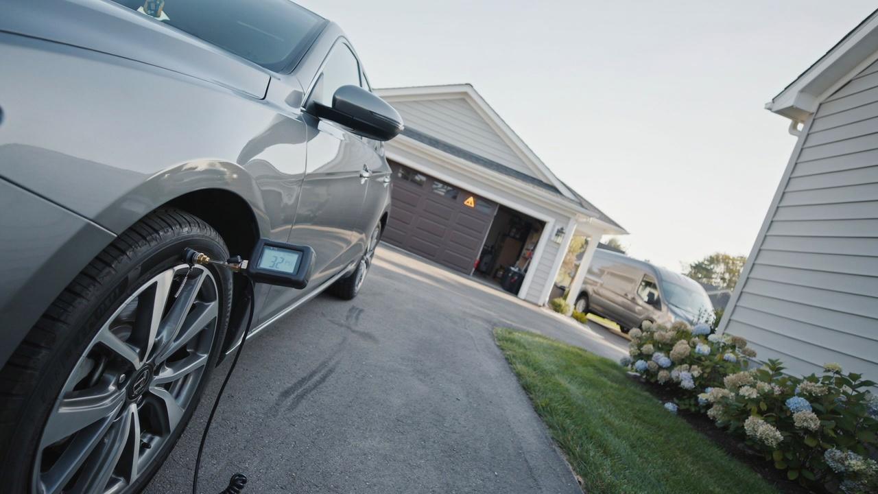 Checking tire pressure with a digital gauge beside a parked car.