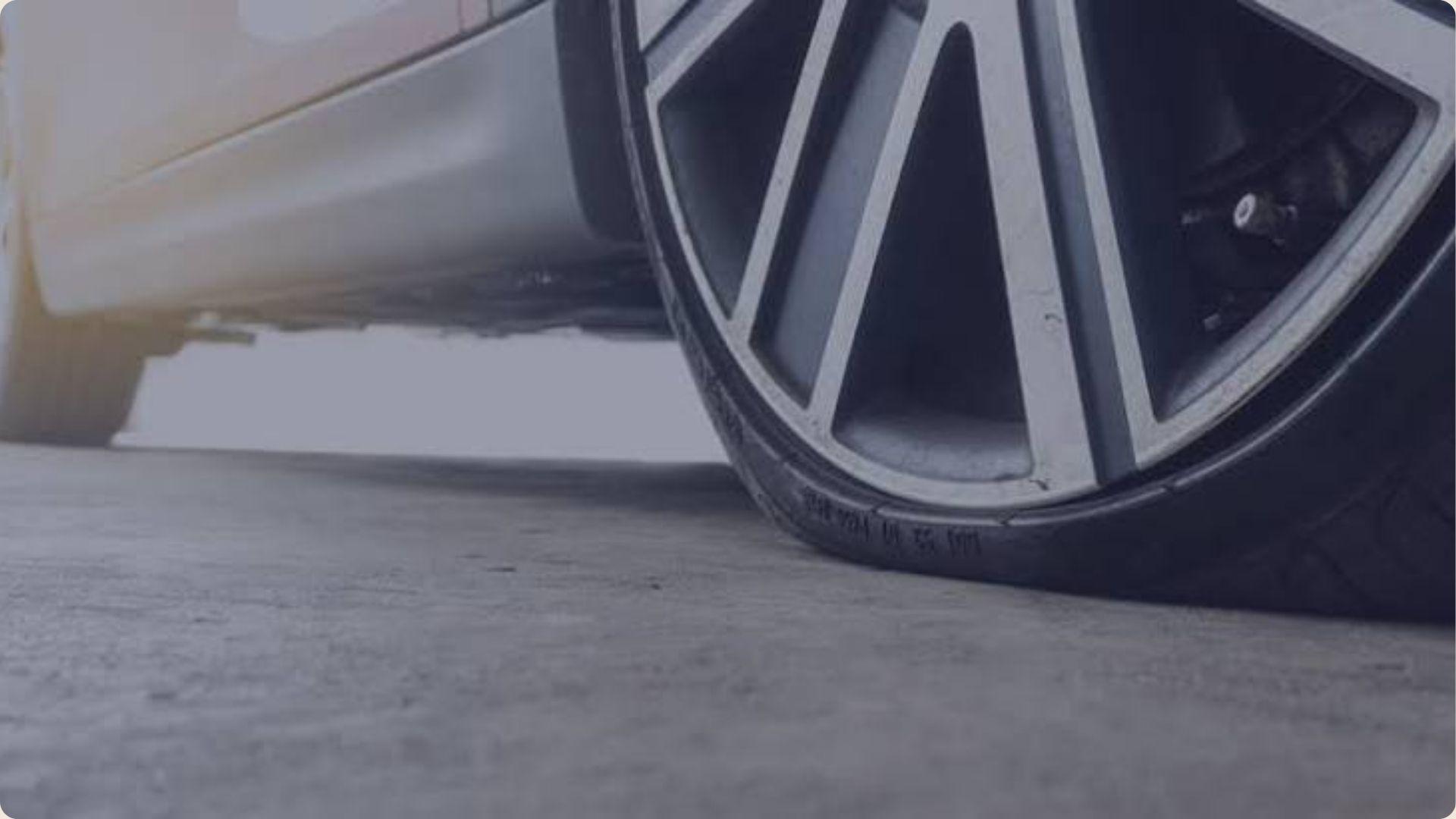 A tire positioned beside a car, highlighting its rubber texture and design against the vehicle's body.