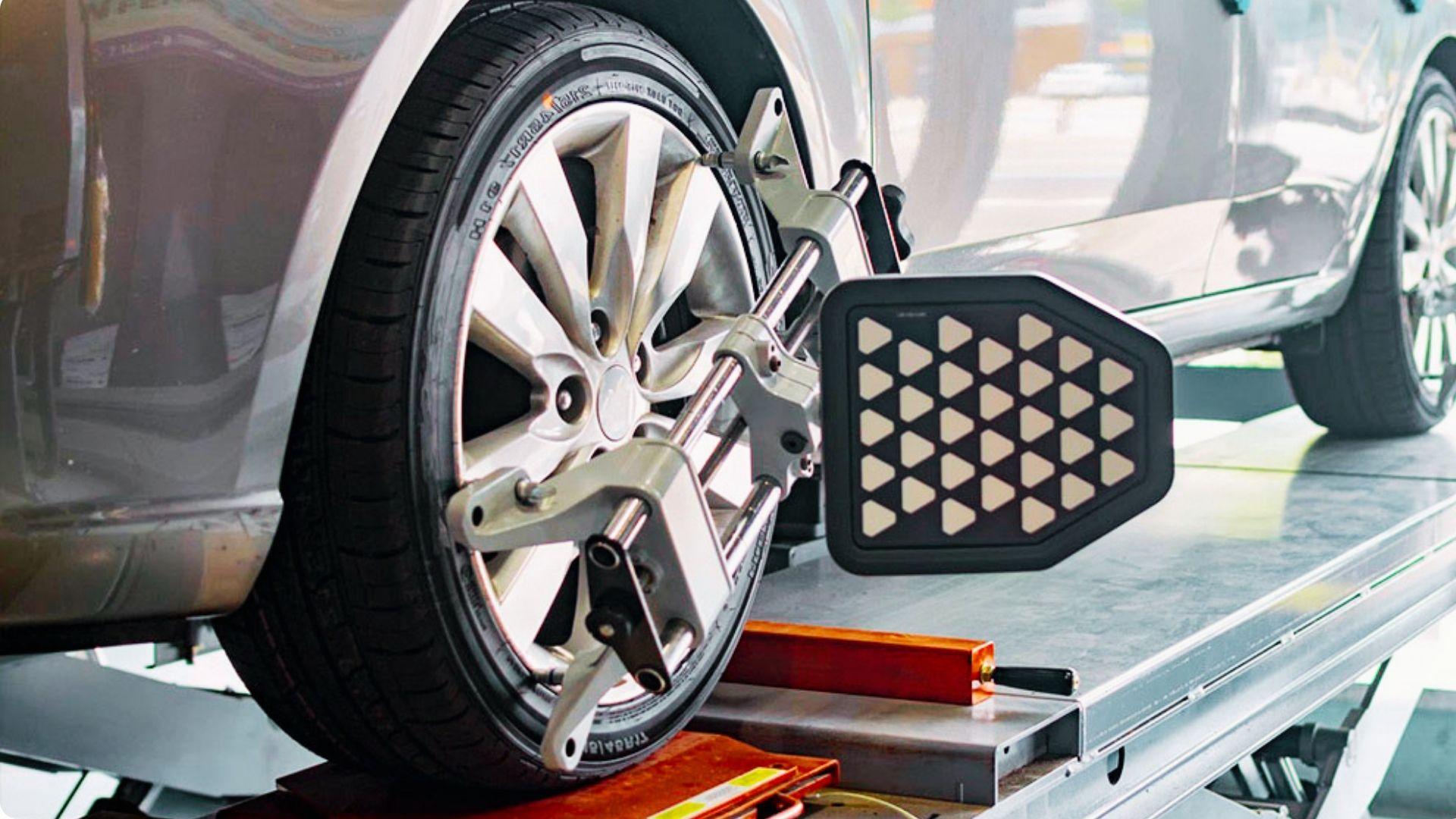 Close-up of car wheel with alignment sensor clamp attached to alloy rim on lift in auto repair shop.