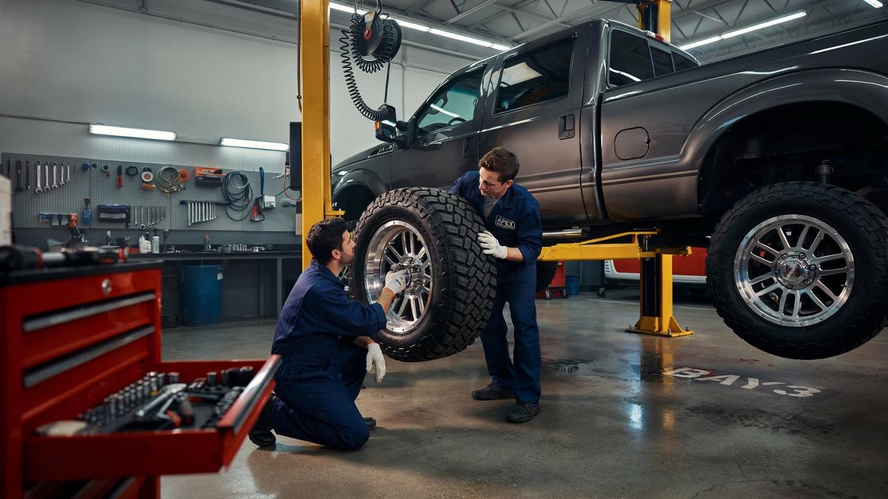 Mechanic performing a tire rotation on a 4x4 pickup truck in a professional garage.